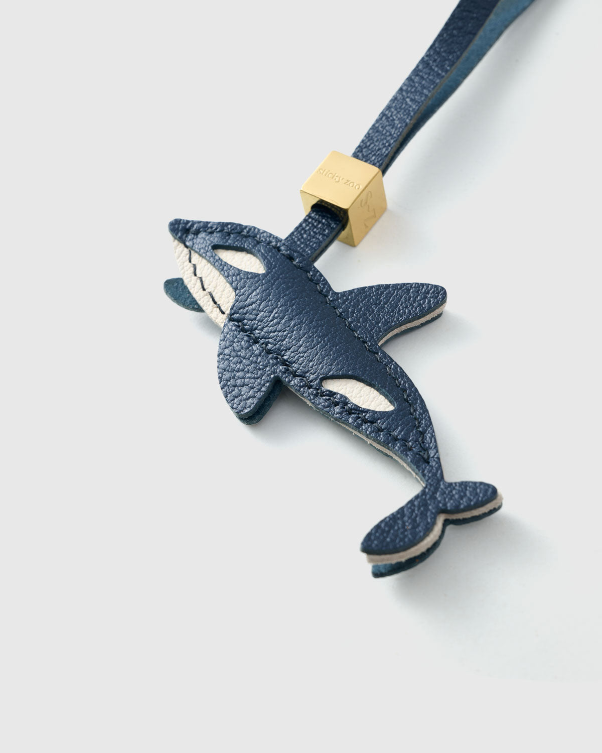 {{Hand-cut. Hand-stitched.}} Close-up of the orca — classic silhouette with hand-stitched white markings across deep navy goatskin. Every panel by hand.