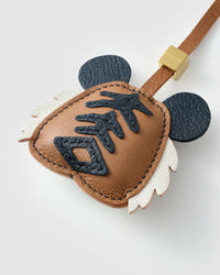 Both editions of the tiger charm — leather strap loop for bags, or 18K gold-plated keychain clip.
