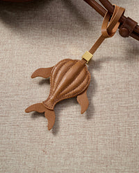 Caramel whale charm styled on a bag, front — a small, specific piece that turns a simple bag into a personal one.