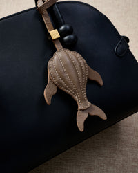 Taupe whale charm styled on a bag, front — a small, specific piece that turns a simple bag into a personal one.