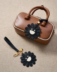 STICKYZOO Night Flower Charm — hand-cut, hand-stitched black petals with smiley face centre in French Alran goatskin. Designed in Amsterdam.