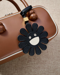 Close-up of STICKYZOO Night Flower Charm — full-grain French Alran goatskin from Tarn, France. Black petals with smiley face centre. 3-day handmade piece.