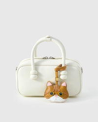 Persian cat charm styled on a cream top-handle bag, front angle — a small, specific piece that turns heads.