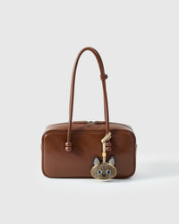 Tonkinese styled on a warm brown leather top-handle bag, front — a small, specific piece that turns a simple bag into a personal one.