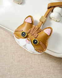 Persian cat charm hanging on a cream top-handle bag, side angle — loved by thousands of cat people. Real French leather, 3 days by hand.