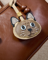Tonkinese charm close on a warm brown leather bag, side angle — 5,000+ reviews across STICKYZOO. Real French leather, 3 days by hand.