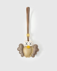 Gold Hootie the Owl charm handmade from French Alran genuine goatskin — metallic gold body, taupe scalloped wings, cream-ringed X-stitched eyes, yellow beak, tan leather strap. Three days by hand. Arrives in luxury gift packaging. Designed in Amsterdam.