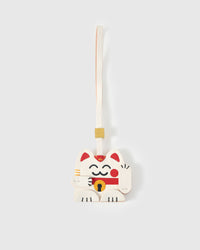 Maneki Neko (lucky cat) charm handmade from French Alran genuine goatskin — white body, red inner ears, raised paw welcoming gesture, gold coin with red detail, smiling face, cream leather strap. Three days by hand. Arrives in luxury gift packaging. Designed in Amsterdam.