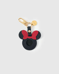Mickey-silhouette AirTag holder handmade from French Alran genuine goatskin — deep black body, red bow at the top, round Mickey ears, precision AirTag cavity, 18K gold-plated keychain clip. Three days by hand. Arrives in luxury gift packaging. Designed in Amsterdam.