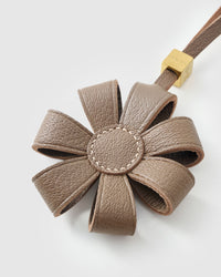 STICKYZOO Daisy Bag Charm clipped to a handbag — handmade French Alran goatskin in warm taupe. 3-day artisan build.