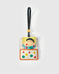 Shinchan cozy-nap charm handmade from French Alran genuine goatskin — the character mid-nap on a cream pillow-bed, teal pyjamas with geometric shape detail, closed eyes, red mouth, dark hair, navy leather strap. Three days by hand. Arrives in luxury gift packaging. Designed in Amsterdam.