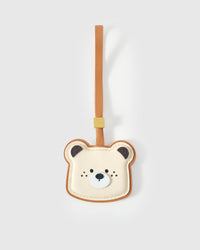 Toast Bear charm handmade from French Alran genuine goatskin — cream ivory face shaped like toast with warm caramel crust edge, dark ears, small stitched eyes and nose, tan leather strap. Three days by hand. Arrives in luxury gift packaging. Designed in Amsterdam.