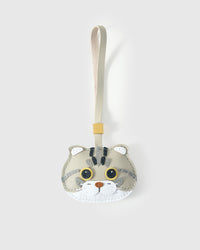 Scottish Fold cat charm handmade from French Alran genuine goatskin leather — sage-grey body, folded ears with white tufts, amber eyes, tabby forehead stripe, cream-sage strap. Three days by hand. Arrives in luxury gift packaging. Designed in Amsterdam.