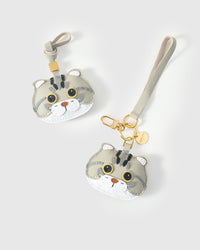 Both editions of the Scottish Fold side by side — leather strap loop for bags, or 18K gold-plated keychain clip with engraved STICKYZOO disc.