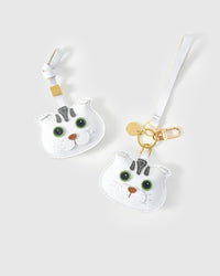 Both editions of the green-eyes Scottish Fold side by side — leather strap loop for bags, or 18K gold-plated keychain clip.