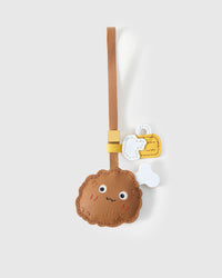 Chicken wing charm handmade from French Alran genuine goatskin — golden-brown crispy body with small stitched face, separate bone-and-napkin detail, tan leather strap. Three days by hand. Arrives in luxury gift packaging. Designed in Amsterdam.