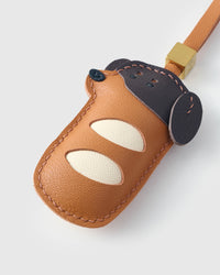 Close-up of handmade Dachshund Sausage Pup leather bag charm — hand-stitched visible edges on French Alran goatskin, soft cream paw detail. STICKYZOO.
