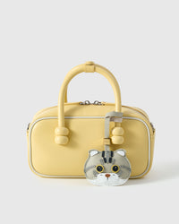 The Scottish Fold styled on a pastel-yellow top-handle bag, front angle — the small piece that turns a simple bag into a personal one.