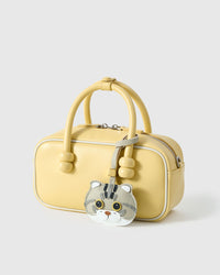 Scottish Fold charm styled on a pastel-yellow bag, side angle — 5,000+ reviews across STICKYZOO. Real French leather, 3 days by hand.