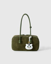 Green-eyes Scottish Fold styled on an olive-green suede top-handle bag, front — a small, specific piece that turns heads.