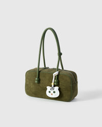 Green-eyes Scottish Fold styled on an olive-green suede top-handle bag, side angle — loved by thousands of cat people. Real French leather, 3 days by hand.