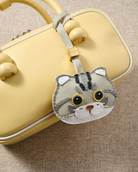 Scottish Fold charm close on a soft-yellow top-handle bag, angled — Real French leather, 3 days by hand.