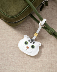 Green-eyes Scottish Fold close on an olive-green leather crossbody, side angle — Real French leather, 3 days by hand.