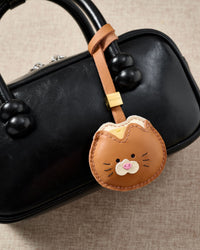 Both editions of the bread kitty charm side by side — leather strap loop for bags, or 18K gold-plated keychain clip with engraved STICKYZOO disc.