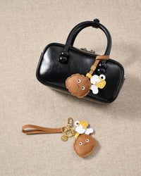 Both editions of the chicken wing charm — leather strap loop for bags, or 18K gold-plated keychain clip.