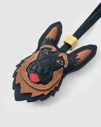 Close-up of handmade German Shepherd leather bag charm — hand-stitched visible edges on French Alran goatskin, hand-layered black-and-tan markings, 18K gold-plated cube hardware. STICKYZOO collectible.