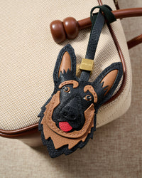 Handmade German Shepherd leather bag charm clipped to a textile handbag — hand-cut feather panels along the neckline, full-grain French Alran goatskin. STICKYZOO collectible.