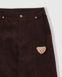 Close-up of plush teddy bear face on brown corduroy fabric showing 3D stuffed texture and embroidered features