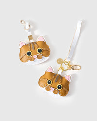 Both editions of the orange tabby side by side — leather strap loop for bags, or 18K gold-plated keychain clip.
