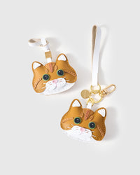 Both editions of the ginger British Shorthair side by side — leather strap loop for bags, or gold-plated keychain clip with engraved disc.