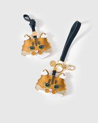 Both editions of the ginger Maine Coon — leather strap loop for bags, or gold-plated keychain clip. Two ways to carry one charm.