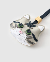 Tight close-up of the Silver Tabby face — green eyes in real leather, charcoal tabby stripes hand-stitched across the forehead, white chin, pink nose. Every panel by hand.
