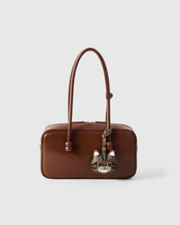 Tabby cat charm styled on a warm brown leather top-handle bag, front — a small, specific piece that turns a simple bag into a personal one.