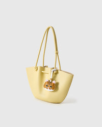 Orange tabby styled on a pastel-yellow tote bag, side angle — real French leather, 3 days by hand.