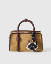 Siamese styled on a tan suede top-handle bag, front — a small, specific piece that turns heads.