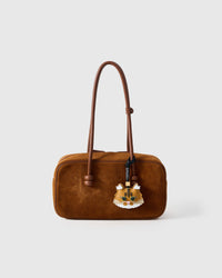 The ginger Maine Coon charm styled on a rich brown suede top-handle bag — the small piece that anchors an outfit.