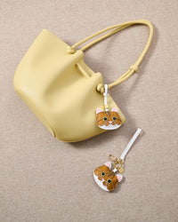 Overhead flatlay — orange tabby charm alongside a pastel-yellow tote and keychain edition. Finished one at a time, by hand.