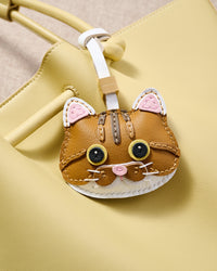 Orange tabby charm close on a pastel-yellow tote, side angle — 5,000+ reviews across STICKYZOO. Real French leather, 3 days by hand.