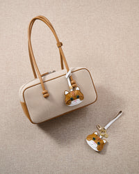 Overhead — ginger British Shorthair charm in strap and keychain editions alongside a cream canvas bag.