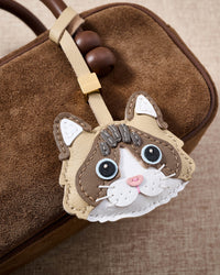 Latte Paws Ragdoll close on a brown suede box bag, side angle — real French leather, 3 days by hand.