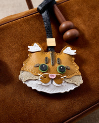 Close-up on brown suede — every layer of the Maine Coon's fluffy cheeks stitched by hand through real French leather. STICKYZOO engraved cube visible.