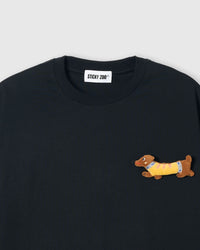 Close-up of plush dachshund applique on black cotton showing stuffed body, yellow sweater, and embroidered face