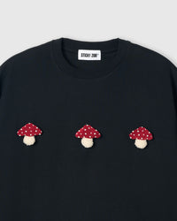 Close-up of plush mushroom applique on black cotton showing red spotted cap and cream stem
