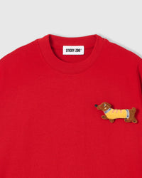 Close-up of plush dachshund applique on red cotton showing stuffed body, yellow sweater, and embroidered face