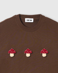 Close-up of plush mushroom applique on brown cotton showing red spotted cap and tonal cream stem