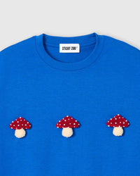 Close-up of plush mushroom on blue cotton showing red spotted cap and cream stem detail